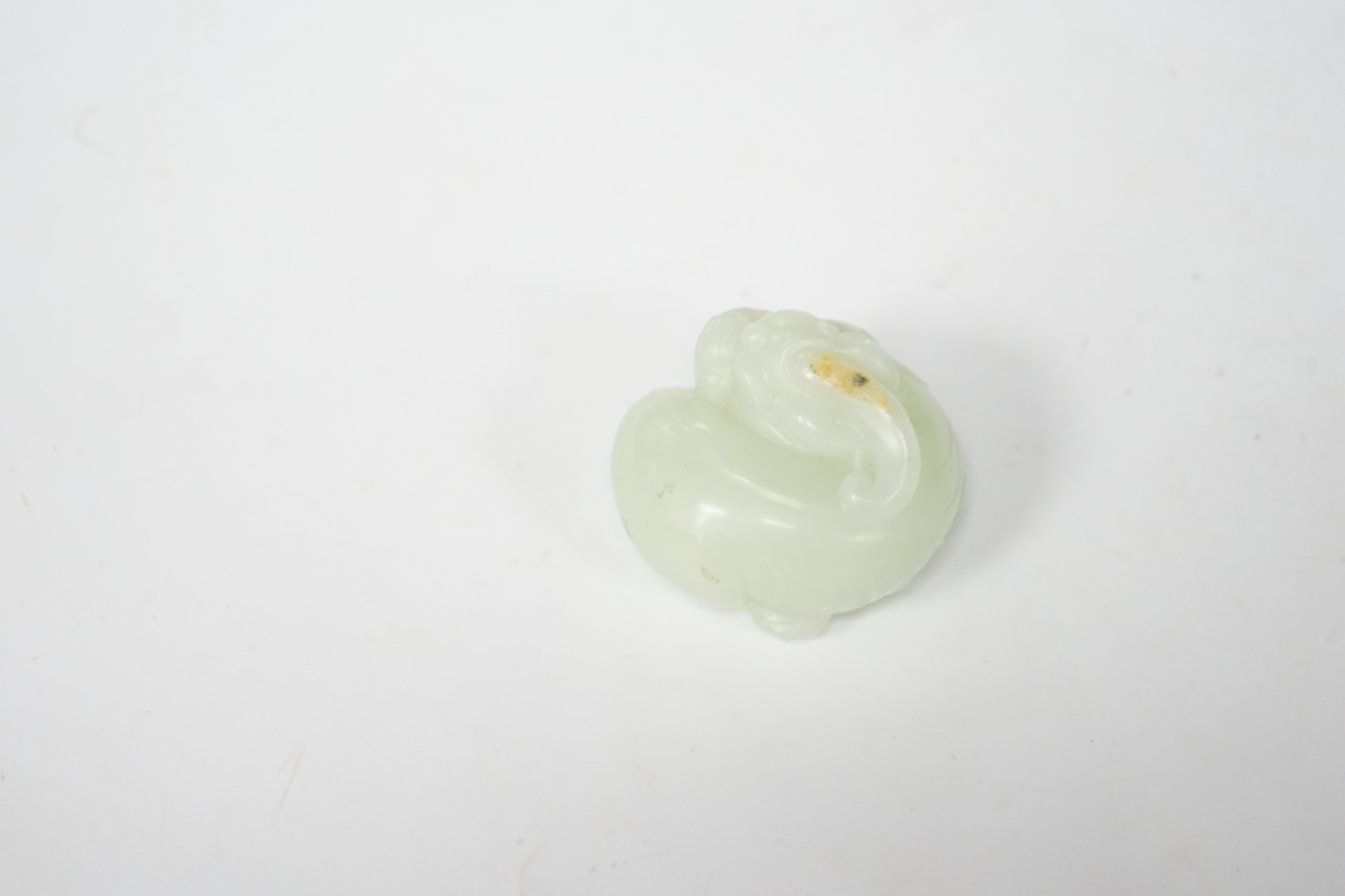 A Chinese celadon jade carving of a lion-dog, in recumbent pose, its crest with a russet inclusion, 5.3cm